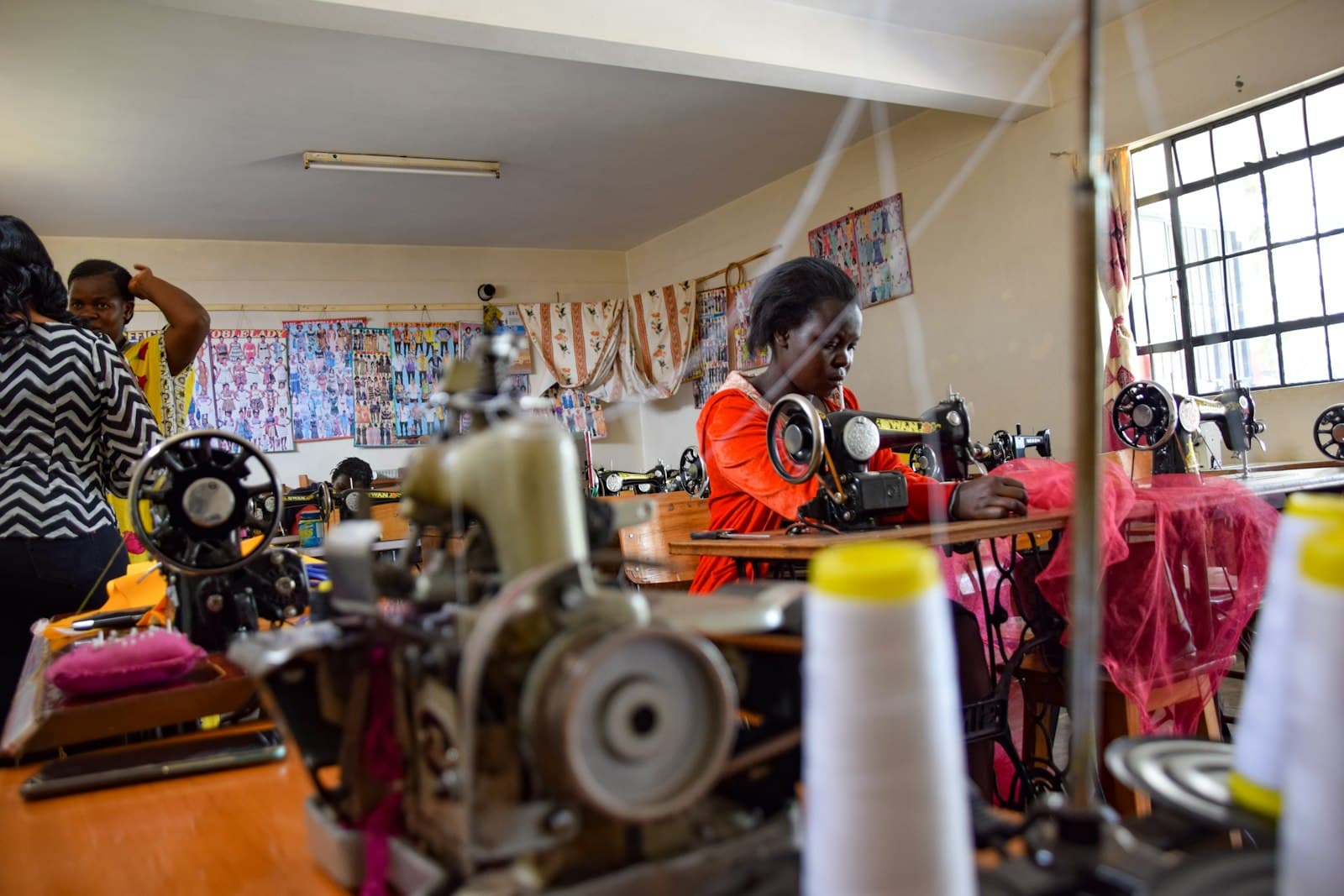 A woman working at a sewing machine in a busy tailoring class