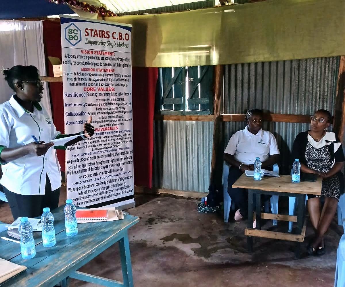 A trainer leading the Monday skills training session beside the STAIRS banner, with two team members seated at a table